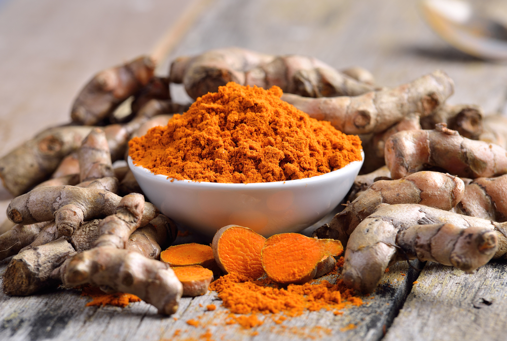 turmeric powder in white dish on wooden background