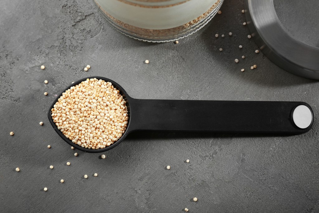 Spoon with quinoa seeds on grey table