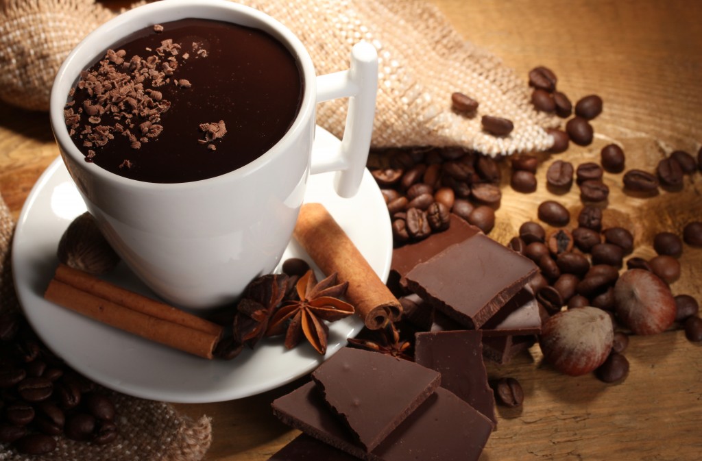 cup of hot chocolate, cinnamon sticks, nuts and chocolate on wooden table