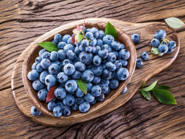 Ripe blueberries in the bowl on the wooden table.