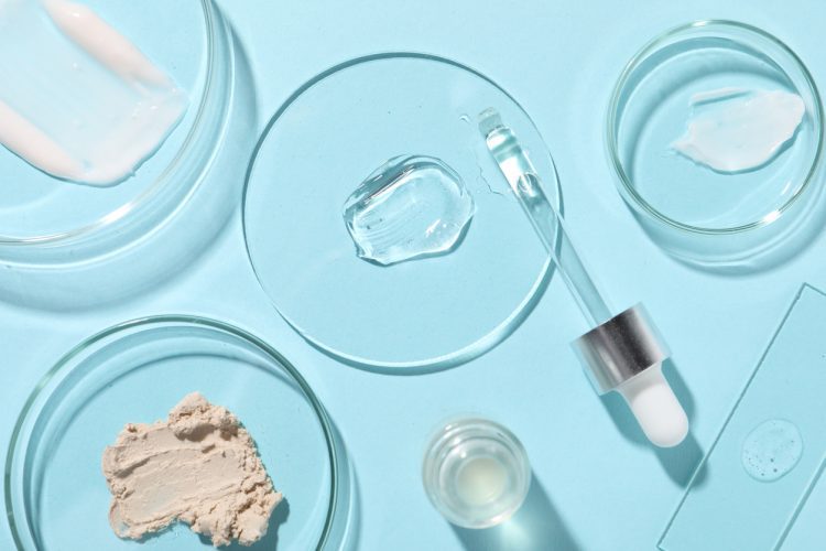 Bottle of cosmetic serum and petri dishes with samples on light blue background, flat lay